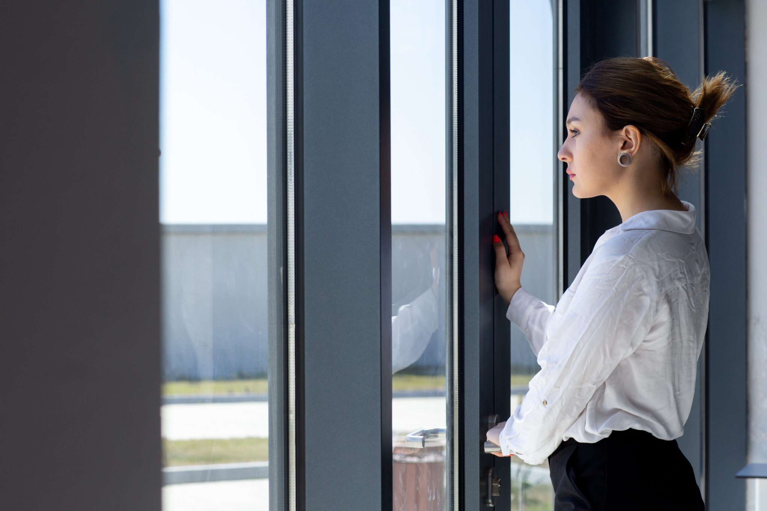 front view young beautiful lady white shirt black trousers looking distance through window hall waiting daytime building job activity